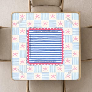 May include: A square tabletop featuring a checkerboard pattern of blue striped squares and cream squares with pink starfish. The center has a blue and white striped square with a scalloped pink border and the text PLAY RIGHT and WALLS LEFT.