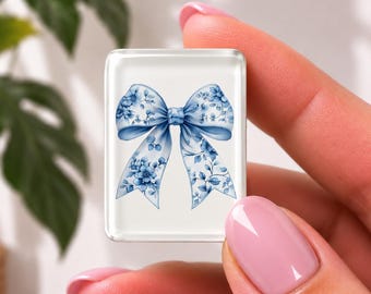 May include: A rectangular tile featuring a white background with a centred blue bow illustration. The bow is decorated with a detailed floral pattern in various shades of blue, including small blossoms and leaves, creating a cohesive design.