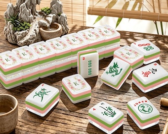 May include: A set of Mahjong tiles featuring white surfaces with green and pink bases. Several tiles display the letter K surrounded by floral wreaths, while others show green dragon illustrations, bamboo stalks, the number 2, the number 9, and the word Joker.