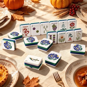May include: A set of white mahjong tiles with green and blue edges, featuring various colorful illustrations including a red dragon, flowers, bamboo, and text such as RED, FLOWER, N, and JOKER, arranged on a light-colored surface with autumn decor.