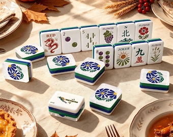 May include: A set of white mahjong tiles with green and blue edges, featuring various colourful illustrations including a red dragon, flowers, bamboo, and text such as RED, FLOWER, N, and JOKER, arranged on a light-coloured surface with autumn decor.