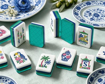 May include: A set of rectangular mahjong tiles featuring white faces with colorful illustrations of a toucan, palm trees, a vase, a leopard labeled Joker, and other symbols. The tiles have translucent teal and dark green layered bases.