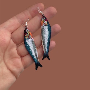 Könnte beinhalten: Ein Paar silberne Ohrhänger mit gestickten Fischen in Blau, Grün, Weiß und Orange.