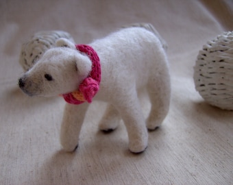 May include: A white felt polar bear wearing a pink and orange crocheted scarf. The bear is standing on a white surface.