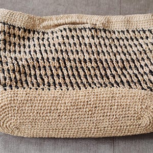 May include: A beige and black woven tote bag with a rectangular shape and a handle. The bag features a woven pattern with alternating beige and black sections. The bottom and top edges are solid beige.