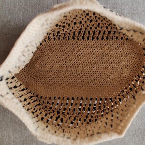 May include: A handmade crochet hat in a neutral color palette. The hat features a beige interior and a cream-colored brim. The open weave design allows for breathability, making it suitable for warm weather. The hat's shape is slightly rounded.