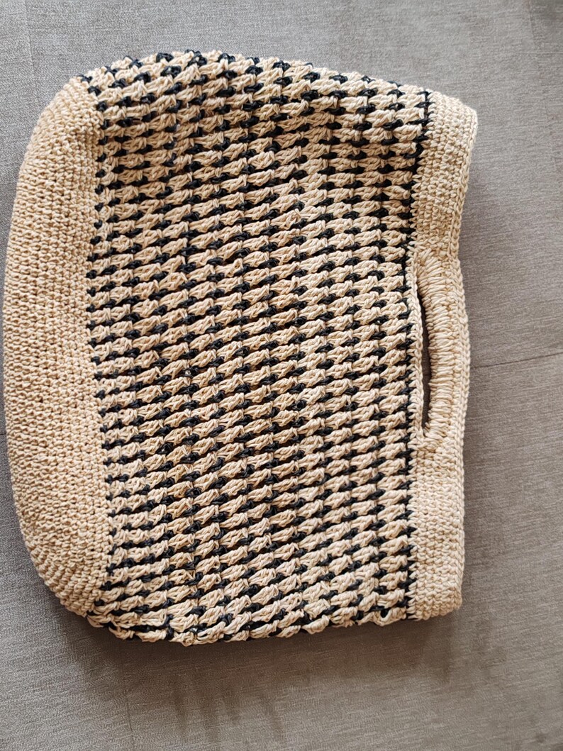 May include: Handmade tote bag with a woven pattern in black and beige. The bag features a rectangular shape with rounded corners and a handle on one side. The woven design creates a textured surface, perfect for carrying essentials.