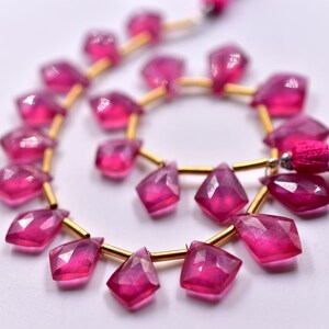 May include: A strand of pink gemstone beads with gold spacers. The beads are faceted and have a teardrop shape. The beads are strung on a gold wire.