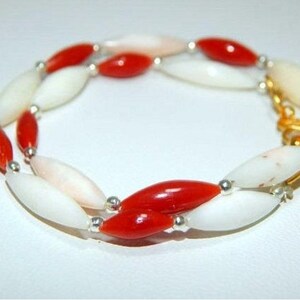 K&ouml;nnte beinhalten: Ein rotes und wei&szlig;es Perlenarmband mit silbernen Akzenten. Die Perlen sind oval geformt und das Armband hat einen Verschluss.