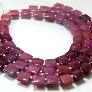 Puede incluir: Una hebra de cuentas de rubí de forma cuadrada en tonos de rosa y morado. Las cuentas están enhebradas en un alambre plateado.