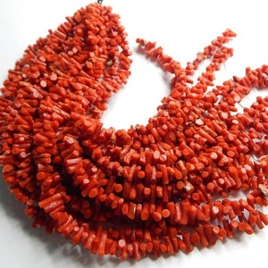 May include: A strand of bright red coral beads, each bead is a small, irregular, branch-like shape. The beads are strung on a thin wire and are ready for jewelry making.