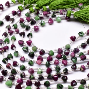May include: A strand of green and pink gemstone beads with silver spacers. The beads are faceted and have a triangular shape. The strand is finished with green tassels.