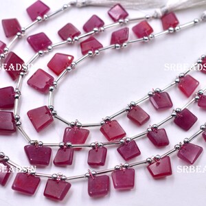 May include: Strands of square, deep red gemstone beads. Each bead is connected by a silver-coloured metal bar and small silver beads. The strands are finished with white tassels. The text "SRBEADSIN" is visible on the image.