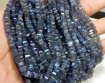 May include: A strand of dark blue labradorite gemstone beads. The beads are square shaped and have a shimmery iridescent finish.