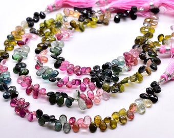 May include: A strand of multi-colored gemstone beads, featuring a variety of shades of pink, green, blue, and black. The beads are faceted and have a teardrop shape. The strand is finished with pink tassels.