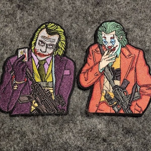 Pode incluir: Dois patches bordados com o personagem Coringa. Um patch mostra o Coringa em um terno roxo segurando uma carta de baralho, o outro em um casaco laranja. Ambos os patches incluem uma arma e estão em um fundo cinza.