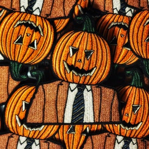 Puede incluir: Un conjunto de parches bordados para planchar que representan una calabaza con traje y corbata. La calabaza tiene una cara de miedo con una amplia sonrisa y dientes afilados. Los parches son de color marrón, naranja y verde.