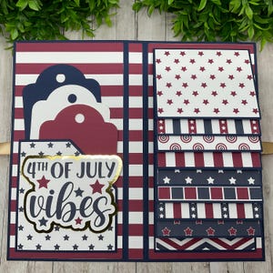 Puede incluir: Un álbum de recortes rojo, blanco y azul con un tema del 4 de julio. La portada presenta un patrón de rayas rojo, blanco y azul con un título "4th of July vibes" de purpurina dorada. El interior del álbum tiene varias páginas con diferentes patrones rojo, blanco y azul.