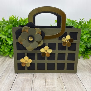 Può includere: Una borsa di carta verde e nera con un manico dorato e decorazioni di fiori dorati. La borsa ha un motivo a griglia.