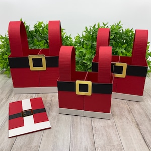 Op de afbeelding: Vier rode en witte kerstman-laarsvormige cadeaudozen met zwarte riemen en gouden gespen. De dozen zijn gemaakt van karton en hebben een feestelijk kerstthema.