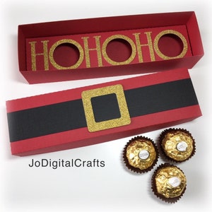 Può includere: Scatola di cartone rossa e nera con una cintura di glitter dorati e le parole "HO HO HO" sul coperchio. La scatola è aperta e sono visibili tre cioccolatini avvolti in oro.