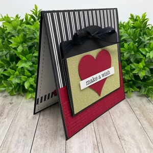 May include: A black and white striped card with a red heart and gold glitter background. The card has a black ribbon and the words "make a wish" on a white banner.
