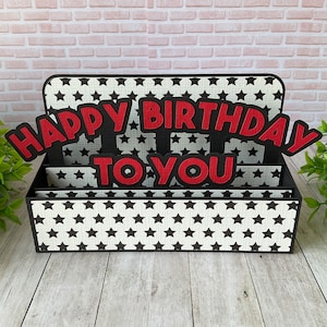 May include: A black and white card box with a pop-up design. The box has a black and white star pattern and says "Happy Birthday To You" in red letters.