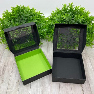 May include: Two black gift boxes with a spiderweb design cut out of the lid. One box has a green interior, the other has a black interior.
