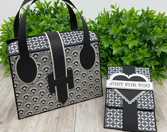 Pode incluir: Uma bolsa de mão com padrão preto e branco com alça preta e um porta-cartões correspondente com o texto "JUST FOR YOU" em branco.