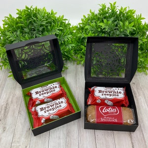 May include: Two black gift boxes with clear lids featuring a spiderweb design. The boxes are filled with chocolate brownie bars and a package of Lotus Speculoos cookies.