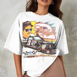 May include: White oversized t-shirt with a vintage-style graphic print of a race car driver, a race car, and the text "Dale Earnhardt" and "Goodwrench Racing Six Time Winston Cup Champion".