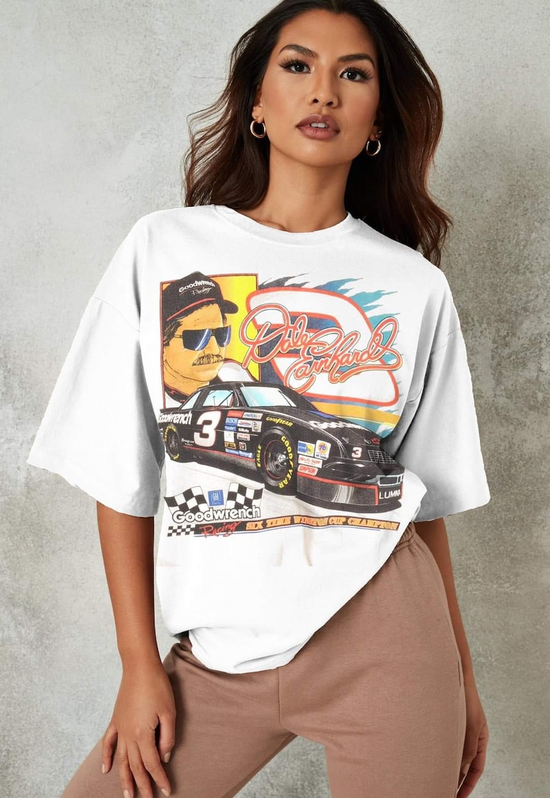 May include: White oversized t-shirt with a vintage-style graphic print of a race car driver, a race car, and the text "Dale Earnhardt" and "Goodwrench Racing Six Time Winston Cup Champion".