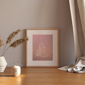 May include: A framed print with a minimalist line drawing of two figures embracing, set against a pink and orange gradient background. The print is displayed on a wooden floor with a vase of dried pampas grass and a small vase of flowers in the foreground.