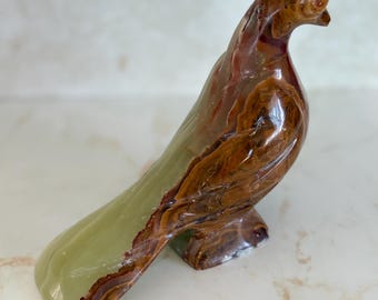May include: A polished stone bird figurine featuring a smooth, glossy finish. The sculpture displays a striking color gradient, transitioning from deep, swirling shades of brown and amber on the head and chest to a pale, translucent light green tail.