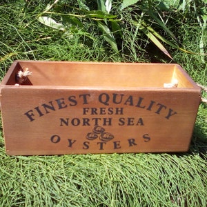May include: A wooden box with rope handles, labeled "FINEST QUALITY FRESH NORTH SEA OYSTERS".