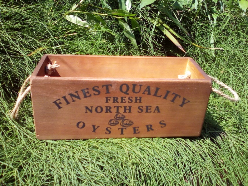 May include: A wooden box with rope handles, labeled "FINEST QUALITY FRESH NORTH SEA OYSTERS".