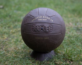 May include: A brown leather soccer ball with the text "Anfield Road L4 The Kop Since 1892" on it.