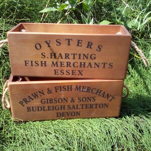 May include: Two wooden crates stacked on top of each other. The top crate is labeled "OYSTERS S. HARTING FISH MERCHANTS ESSEX". The bottom crate is labeled "PRAWN & FISH MERCHANT GIBSON & SONS BUDLEIGH SALTERTON DEVON".