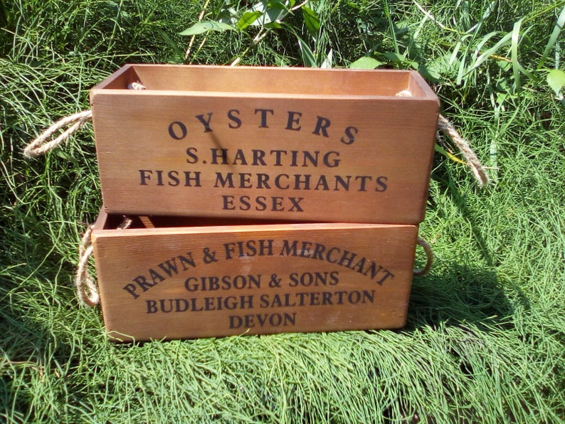 May include: Two wooden crates stacked on top of each other. The top crate is labeled "OYSTERS S. HARTING FISH MERCHANTS ESSEX". The bottom crate is labeled "PRAWN & FISH MERCHANT GIBSON & SONS BUDLEIGH SALTERTON DEVON".
