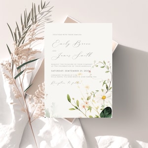 May include: Wedding invitation with a floral design featuring white flowers and green leaves. The invitation is for Emily Brown and James Smith, and the wedding is scheduled for Saturday, September 23, 2023.