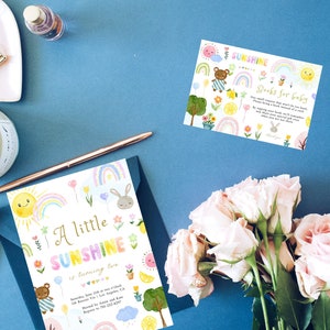 May include: A colorful baby shower invitation with a rainbow, sun, bunny, and teddy bear. The invitation reads "A little sunshine is turning two".