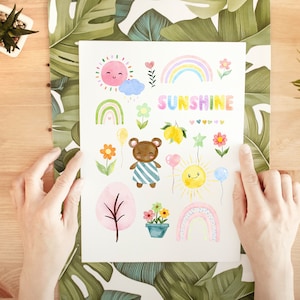 May include: A white card with watercolor illustrations of a bear, flowers, rainbows, suns, and lemons. The text "SUNSHINE" is written in rainbow colors.