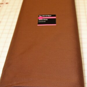 Puede incluir: Un rollo de tela Dream Cotton de color marr&oacute;n, de 45 pulgadas de ancho, 100% algod&oacute;n peinado. La tela est&aacute; etiquetada con "Color: Brown" y "23 yds".