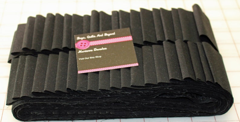 May include: A stack of black fabric strips, possibly for quilting or crafting. A business card with the text "Bags, Quilts And Beyond" and "Marianne Darahus" is visible. The fabric is folded in a layered pattern.