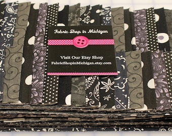 May include: A stack of fabric strips in various black, gray, and white patterns. The patterns include floral, polka dots, and paisley designs. A business card with the text "Fabric Shop in Michigan" is on top.