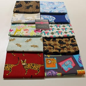 Puede incluir: Una colección de 10 cuadrados de tela con varios estampados de animales. Los estampados incluyen elefantes, tigres, jirafas, gatos y ciervos. Las telas son de varios colores, incluyendo azul, verde, marrón, rojo y blanco. El texto "Wild Spirit" es visible en uno de los cuadrados.