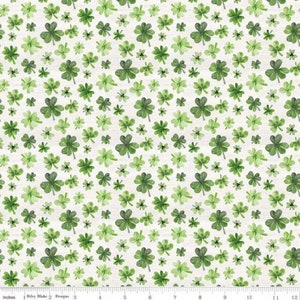 May include: A white fabric with a repeating pattern of green four-leaf clovers of varying sizes. The clovers are painted in a watercolor style, giving them a soft, slightly blurred appearance.