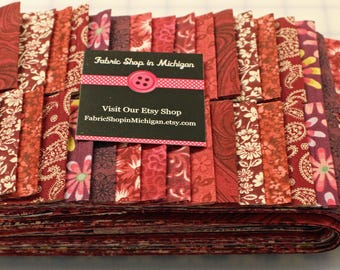 May include: A stack of red fabric strips with various floral and paisley patterns. A business card with the text "Fabric Shop in Michigan" and the Etsy shop URL is on top of the fabric.