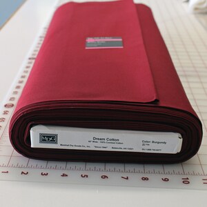 May include: A roll of burgundy red Dream Cotton fabric, 45 inches wide and 100% combed cotton. The fabric is made by Marshall Dry Goods Co., Inc. and is available in 25 yard increments.