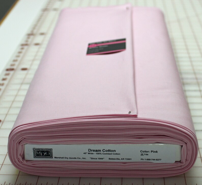 May include: A rolled bolt of pink Dream Cotton fabric, 45 inches wide, made of 100% combed cotton. The label indicates the color is pink and the bolt contains 25 yards of fabric. The fabric is from Marshall Dry Goods Co., Inc.